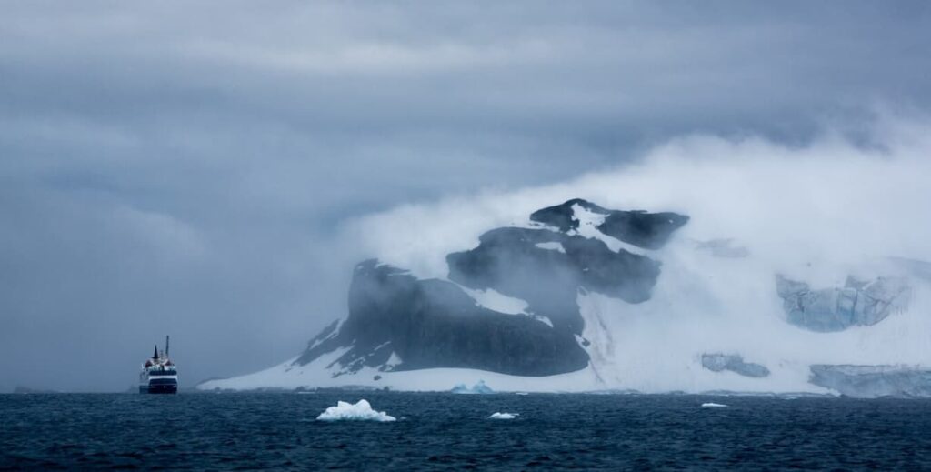 Ship facing misty Antarctic mountains among icebergs