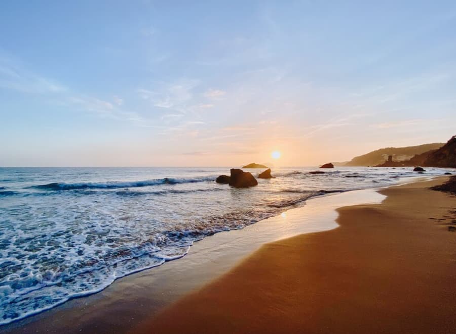 Sun dips over the horizon at a serene beach with rocks